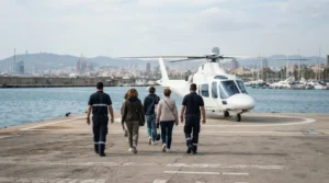 Passengers seen from behind walking with ground crew towards a plain helicopter on a waterfront helipad in Barcelona