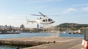 A plain helicopter lifting off from a waterfront helipad in Barcelona, with the city and Montjuic behind in soft light