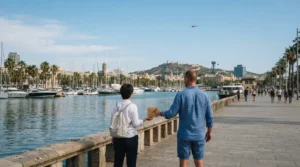 Two people on the Port Vell promenade, one handing an envelope, a helicopter in the sky above the harbour and Montjuic